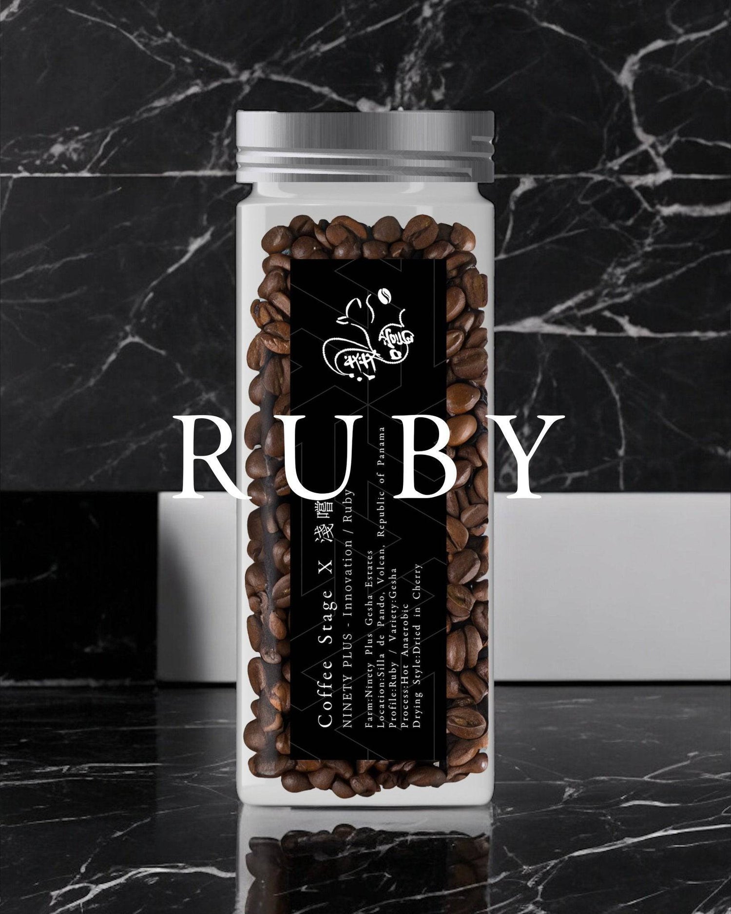 Clear glass jar filled with dark roasted coffee beans, labeled "RUBY" in large white text, set against a black marble background. The jar features a black label with white text and a small logo.