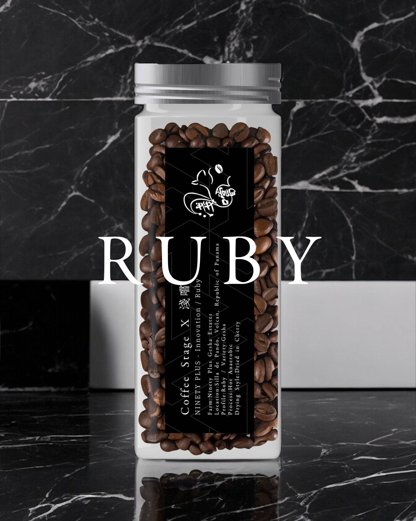 Clear glass jar filled with dark roasted coffee beans, labeled "RUBY" in large white text, set against a black marble background. The jar features a black label with white text and a small logo.
