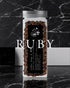 Clear glass jar filled with dark roasted coffee beans, labeled "RUBY" in large white text, set against a black marble background. The jar features a black label with white text and a small logo.