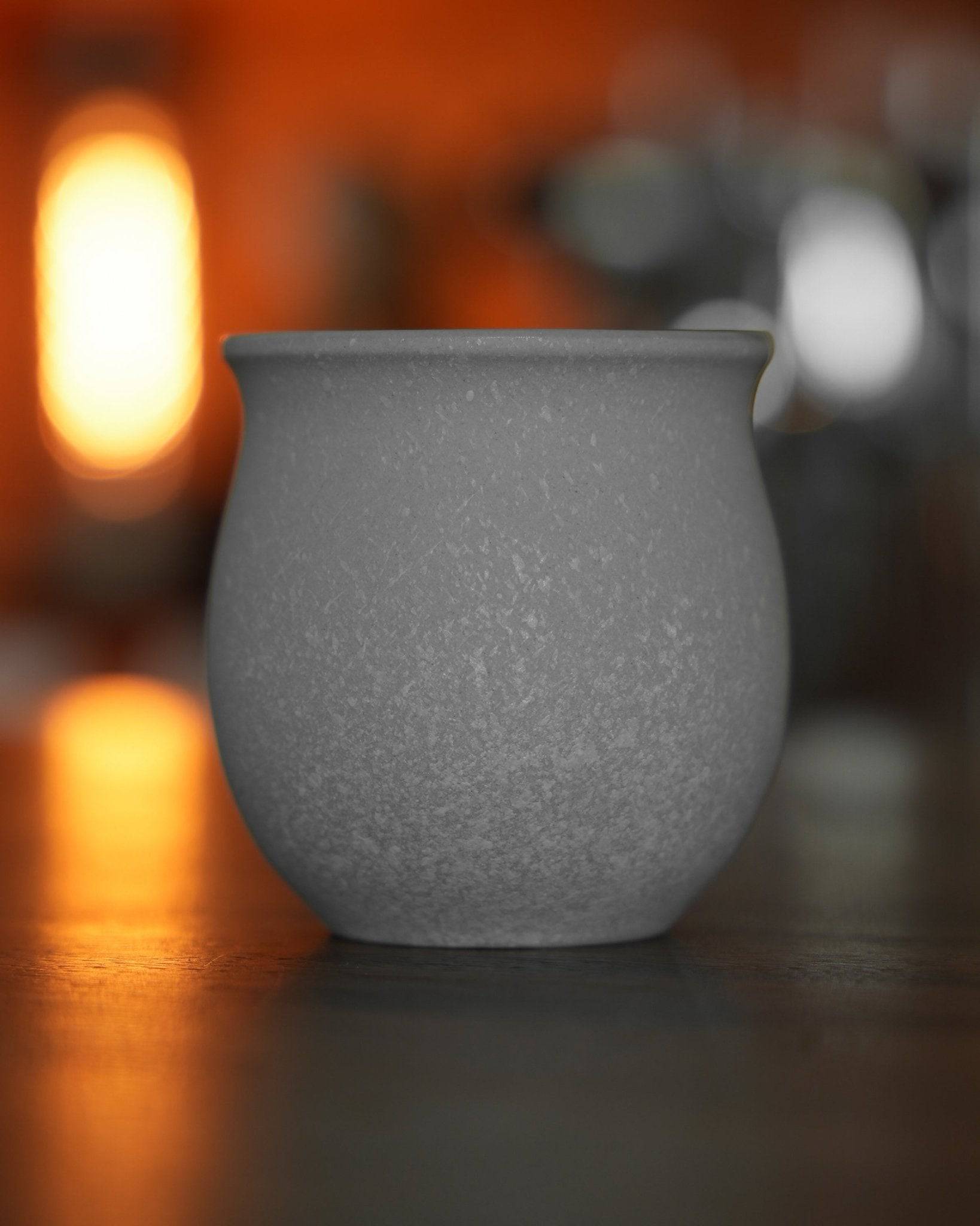Ninety Plus Coffee Savour Cup in basalt white, featuring a textured matte finish and rounded shape, displayed on a reflective surface with warm ambient lighting, showcasing its elegant design inspired by volcanic rocks.