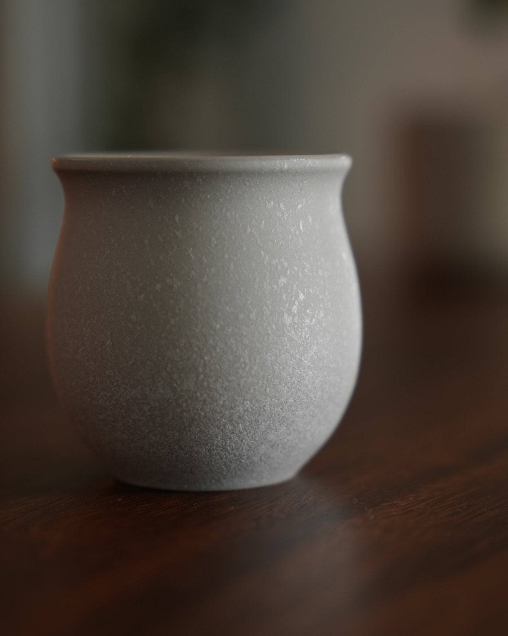 Ninety Plus Coffee Savour Cup in Basalt white, a textured ceramic cup with a curved shape on a wooden surface, designed for premium coffee tasting inspired by volcanic soil