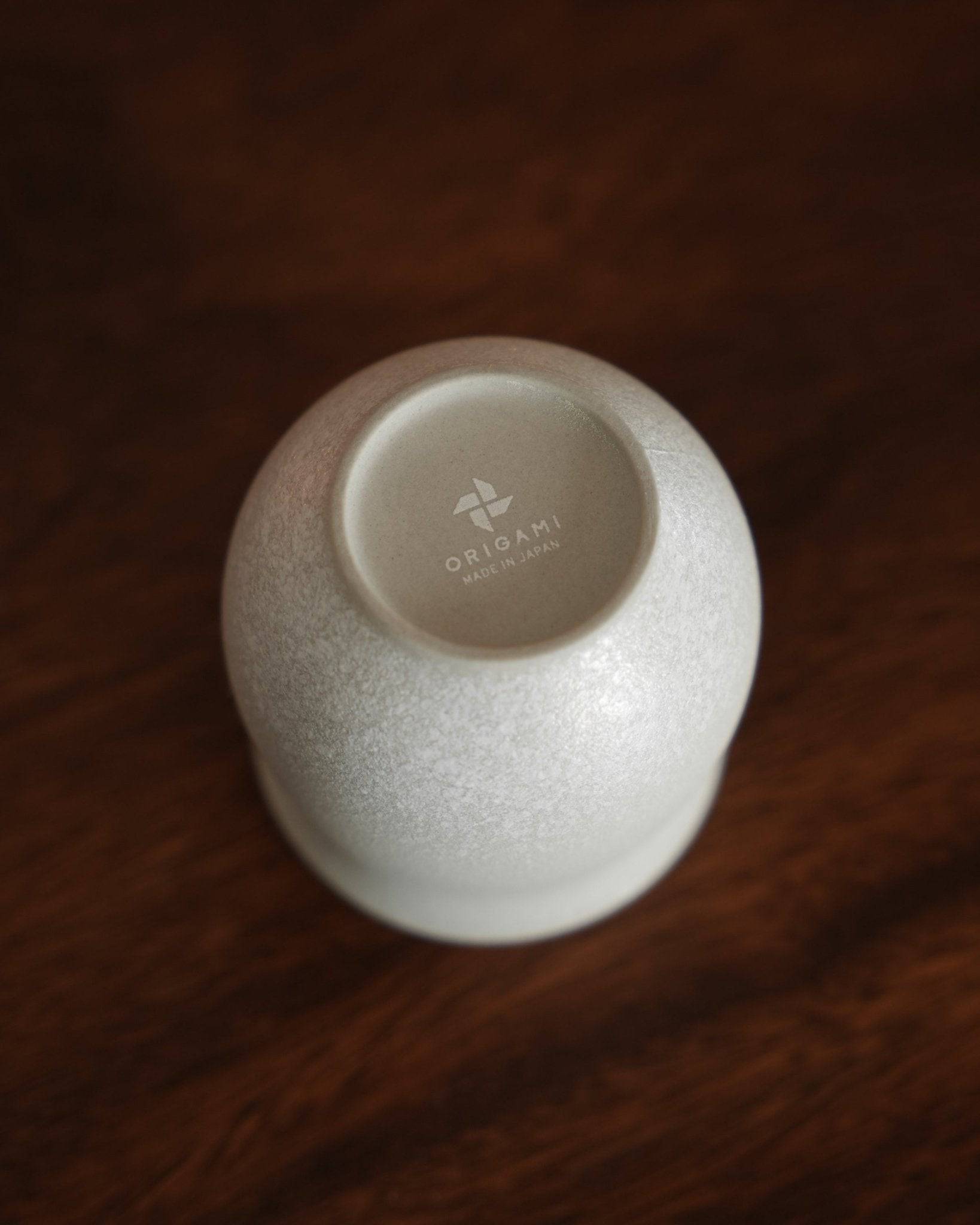 Ninety Plus Coffee Savour Cup 10.1 in Basalt white, designed by Origami, showcasing its unique shape and texture on a dark wooden surface. The cup&