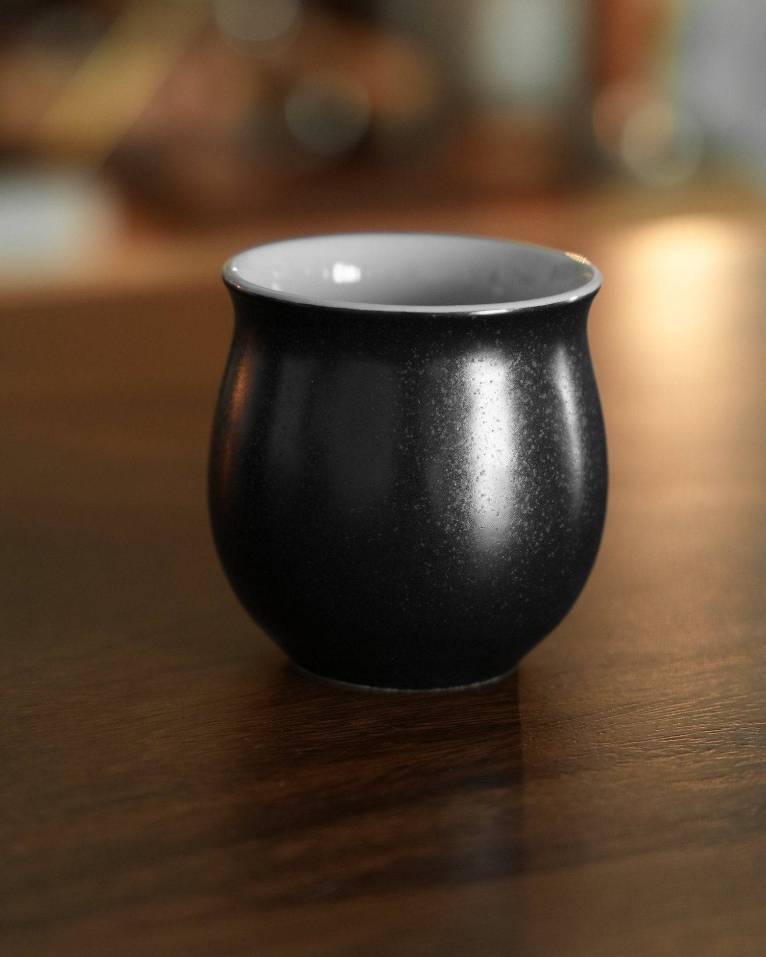 Ninety Plus Coffee Savour Cup 10.1 in obsidian black, showcasing its elegant curved shape and matte exterior finish, sitting on a wooden surface with a soft background blur, highlighting its premium design for specialty coffee tasting