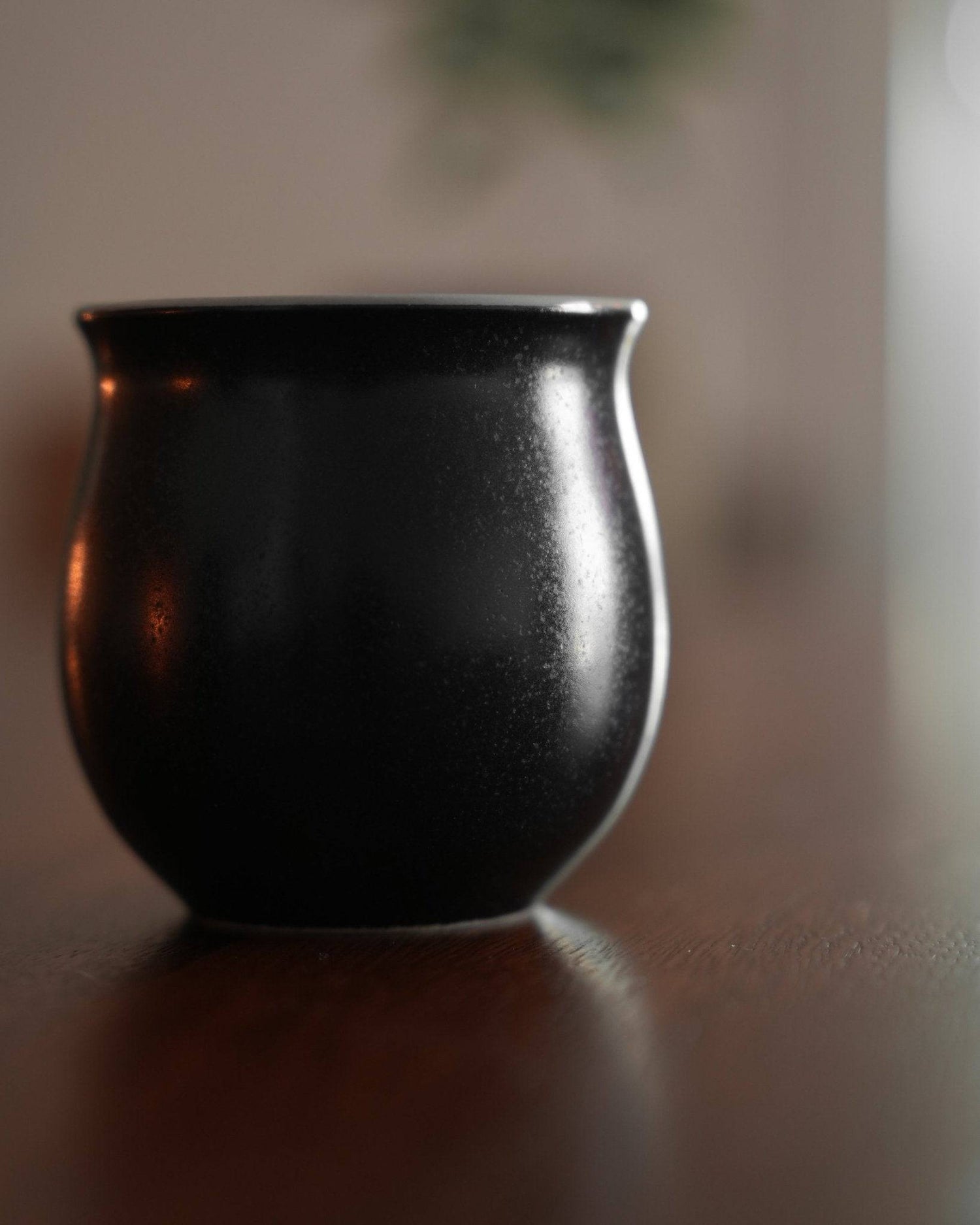 Elegant black Ninety Plus Savour Cup on wooden surface, inspired by obsidian. Curved shape with slight sheen, designed for specialty coffee tasting. Reflects natural aesthetics and Baru Volcano&