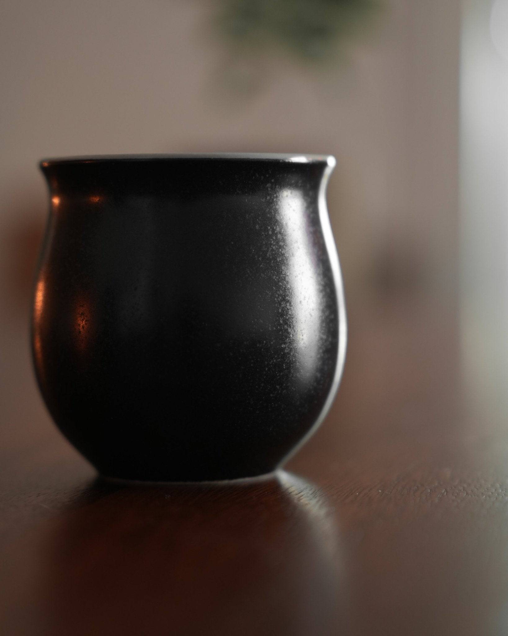 Elegant black Ninety Plus Savour Cup on wooden surface, inspired by obsidian. Curved shape with slight sheen, designed for specialty coffee tasting. Reflects natural aesthetics and Baru Volcano&