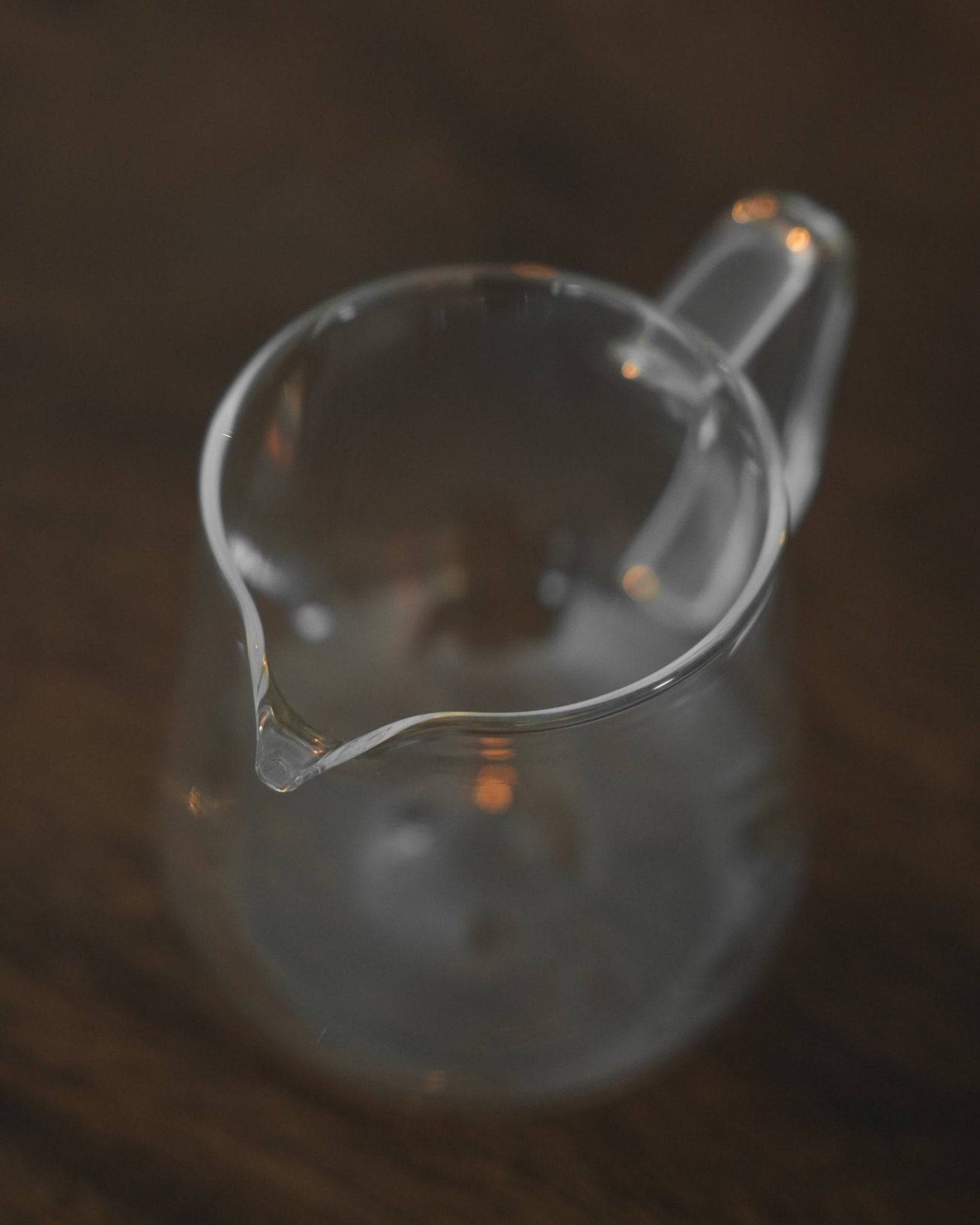 Transparent glass coffee serving pitcher by Ninety Plus, designed for precise pour-over brewing and elegant sharing of premium coffee, compatible with Origami drippers, on a dark wooden surface