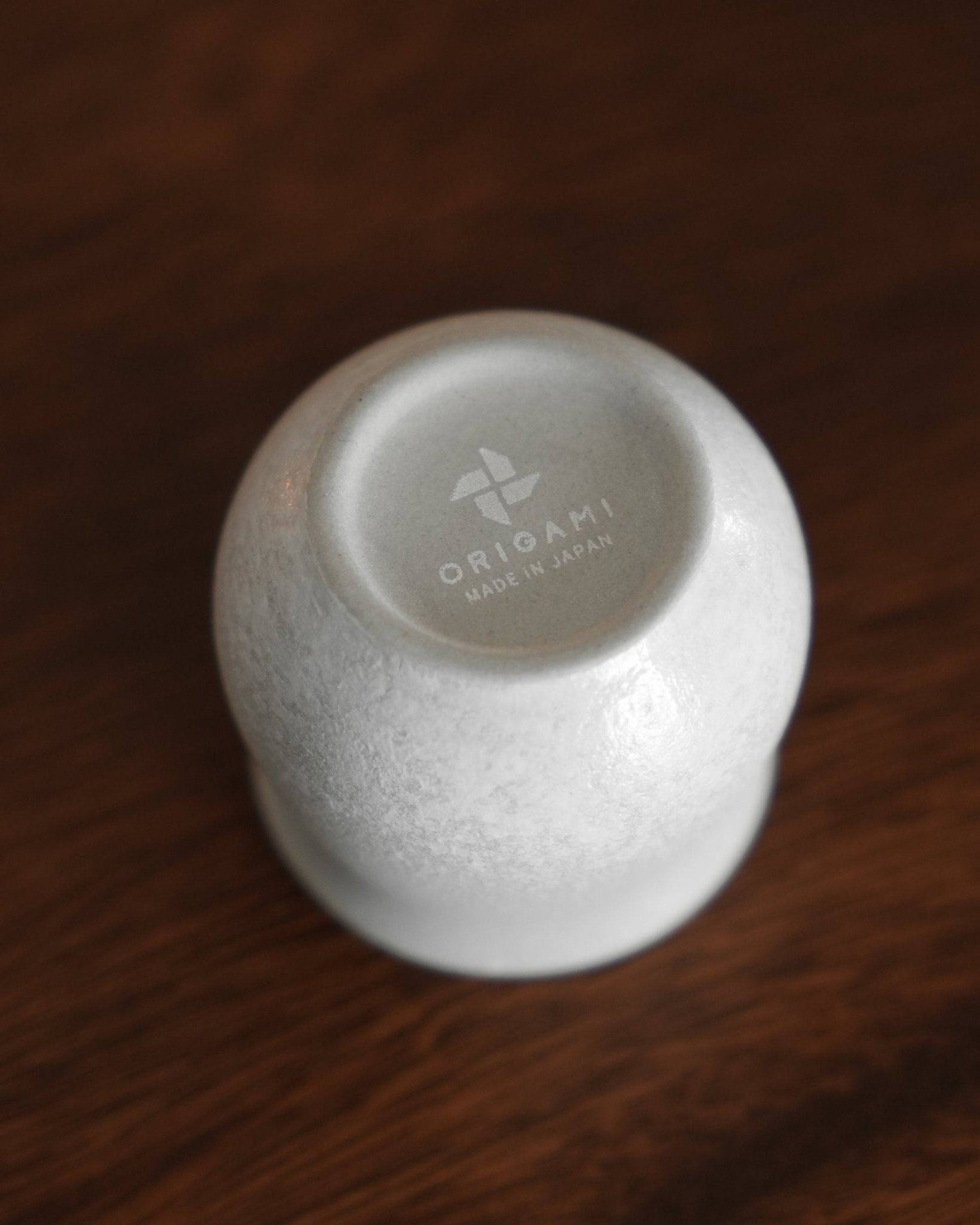 Inverted white ceramic cup from Ninety Plus Coffee Sharing Set, displaying Origami brand logo and &