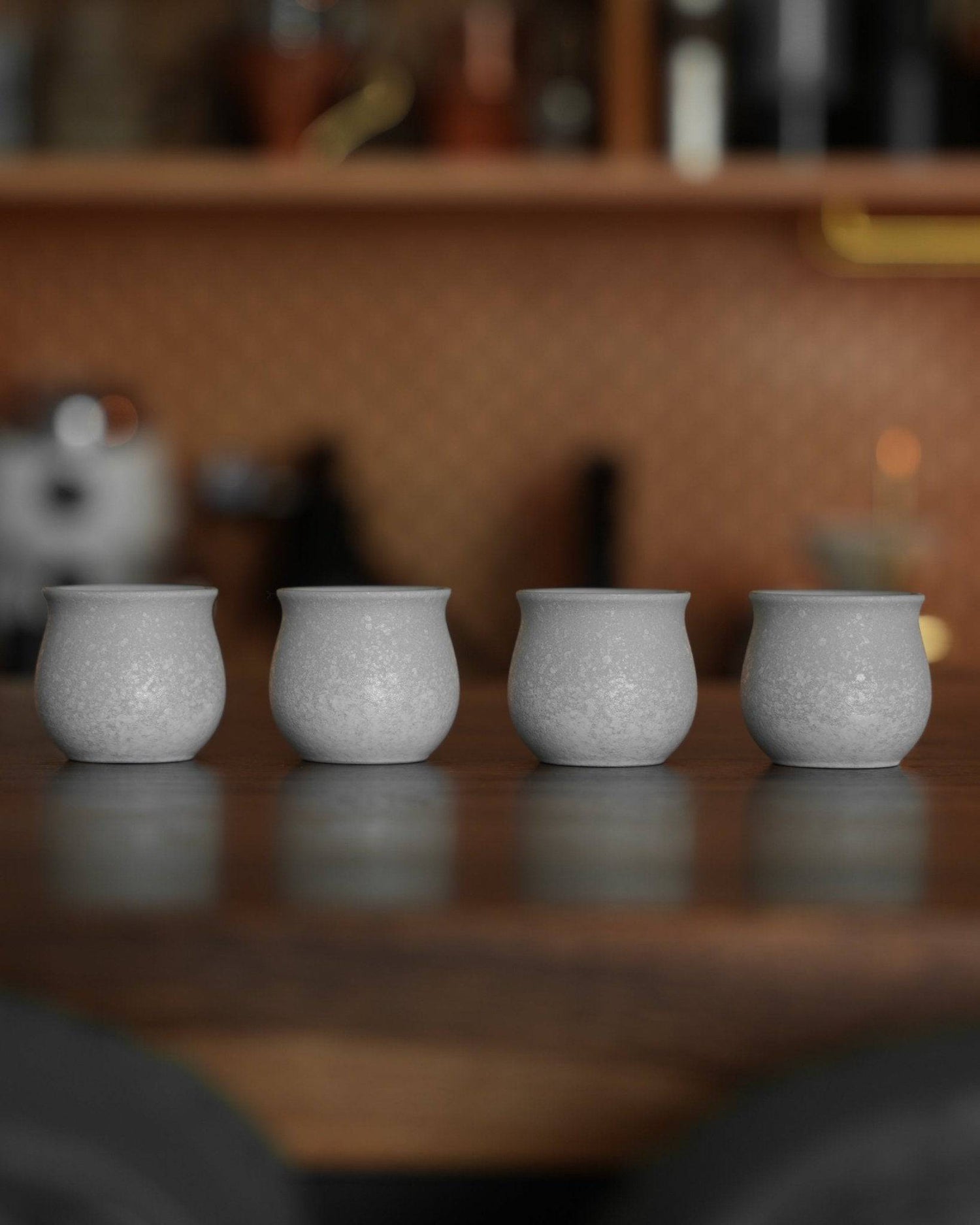 Four elegant white ceramic cups from Ninety Plus Coffee Sharing Cup Set arranged in a row on a wooden surface, showcasing their unique textured finish and curved shape for premium coffee tasting experience.