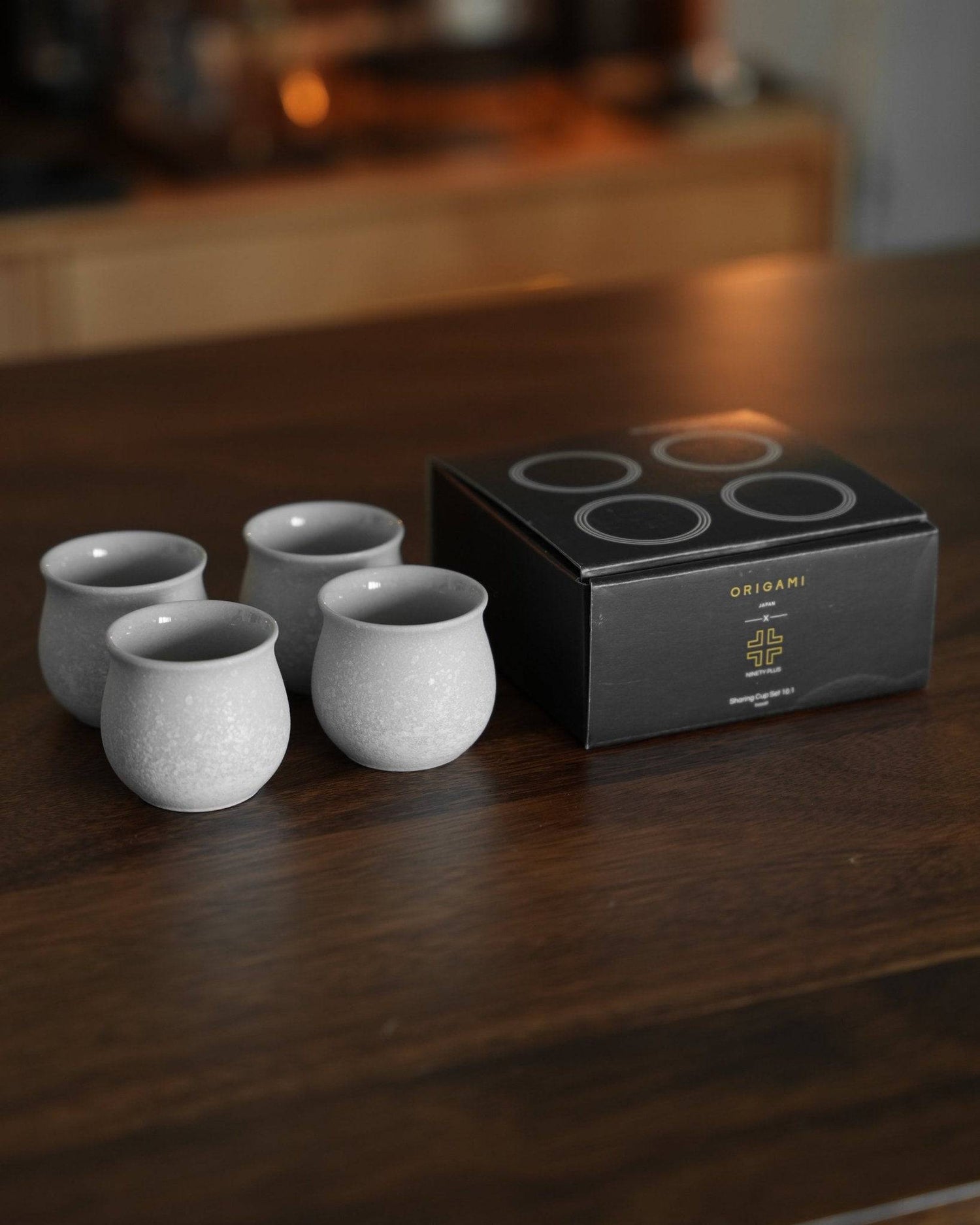 Ninety Plus Coffee Sharing Cup Set featuring four light gray ceramic cups and a black packaging box on a wooden surface, showcasing elegant design for premium coffee experience
