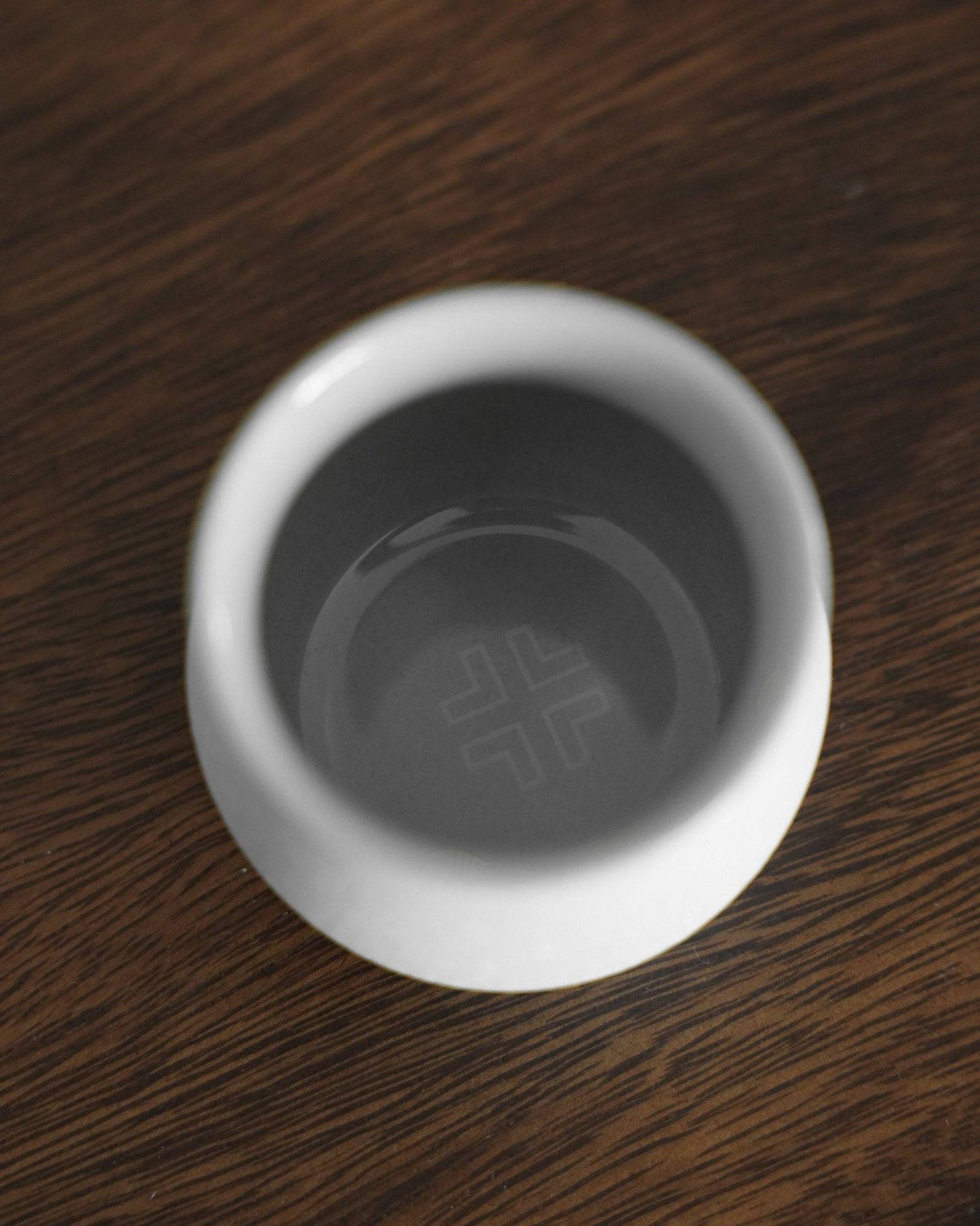 Ninety Plus Coffee Sharing Cup in Basalt white, overhead view on dark wood surface, showcasing minimalist design with engraved logo at the bottom