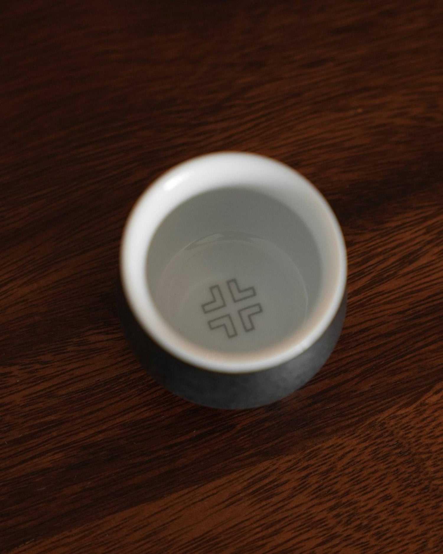 Ninety Plus Coffee Sharing Cup Set Obsidian edition, single white ceramic cup with minimalist logo on dark wooden surface, showcasing elegant design for premium coffee sharing experience