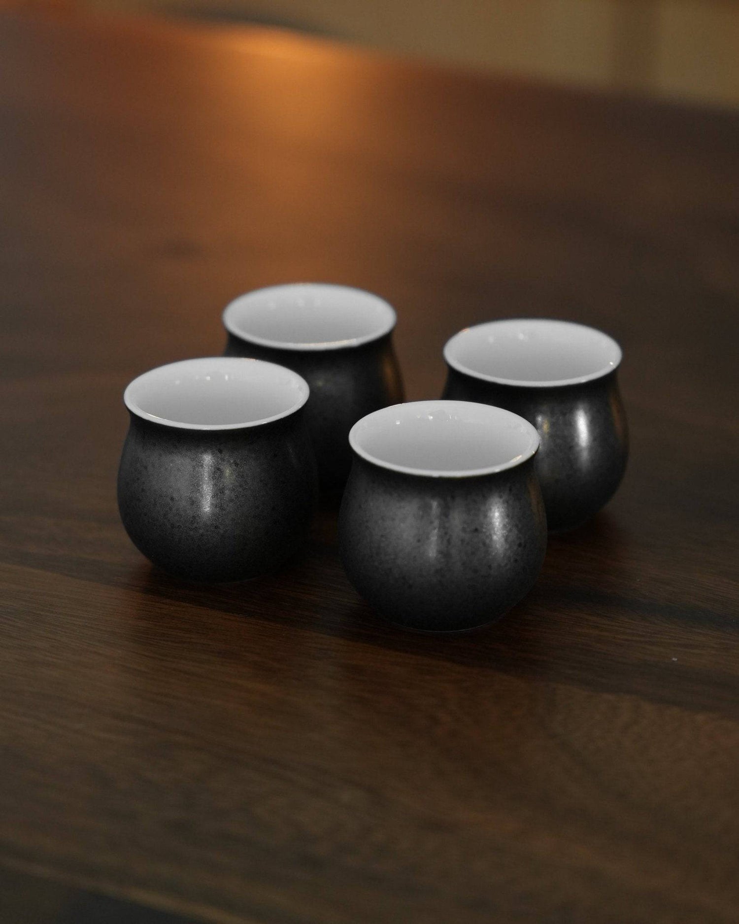 Ninety Plus Coffee Sharing Cup Set featuring four elegant black obsidian cups with white interiors on a wooden surface, perfect for sharing premium coffee experiences with friends