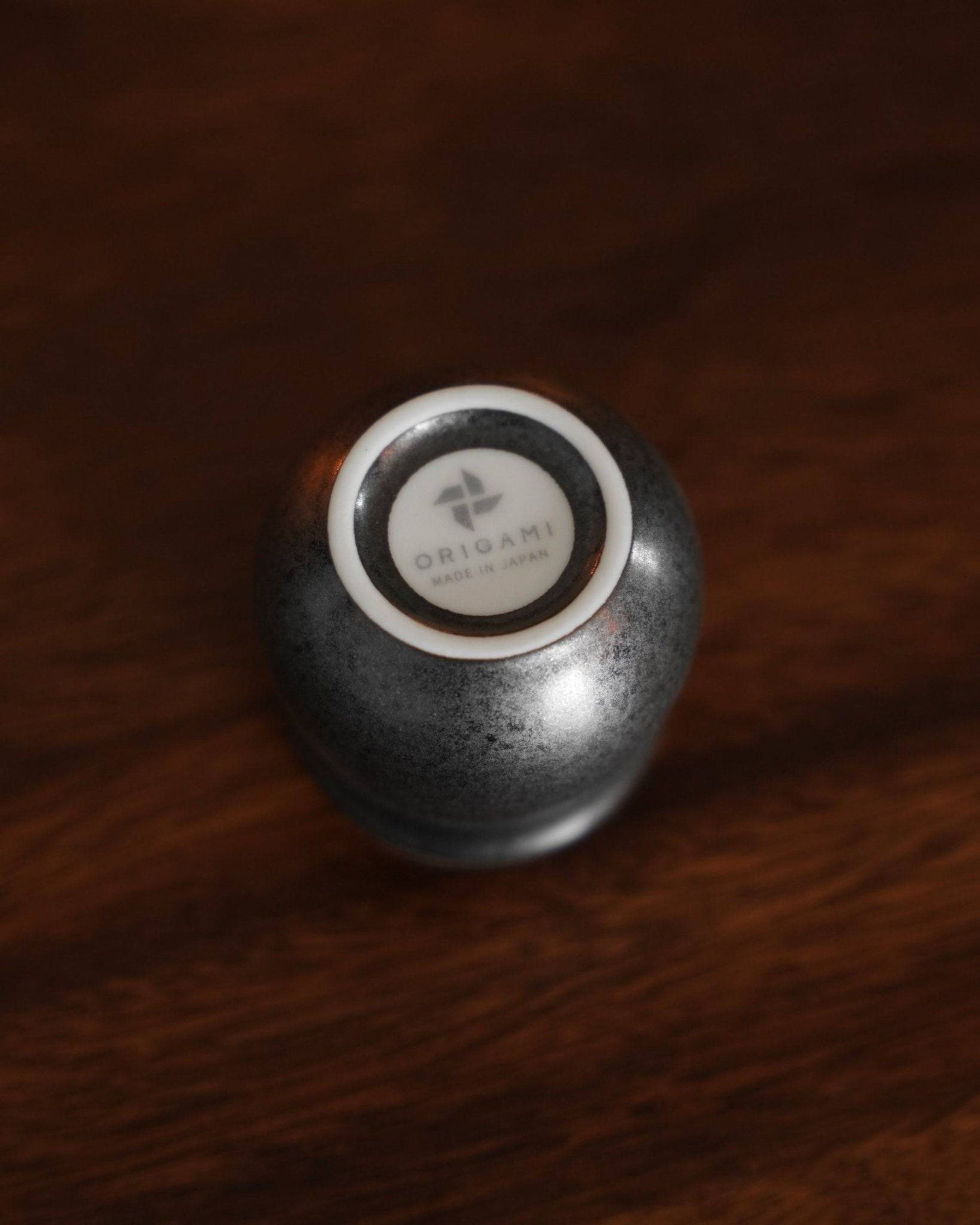 Sleek black ceramic cup from Ninety Plus Coffee Sharing Set, featuring Origami logo on bottom, placed on dark wooden surface, showcasing elegant design and premium quality for coffee enthusiasts.