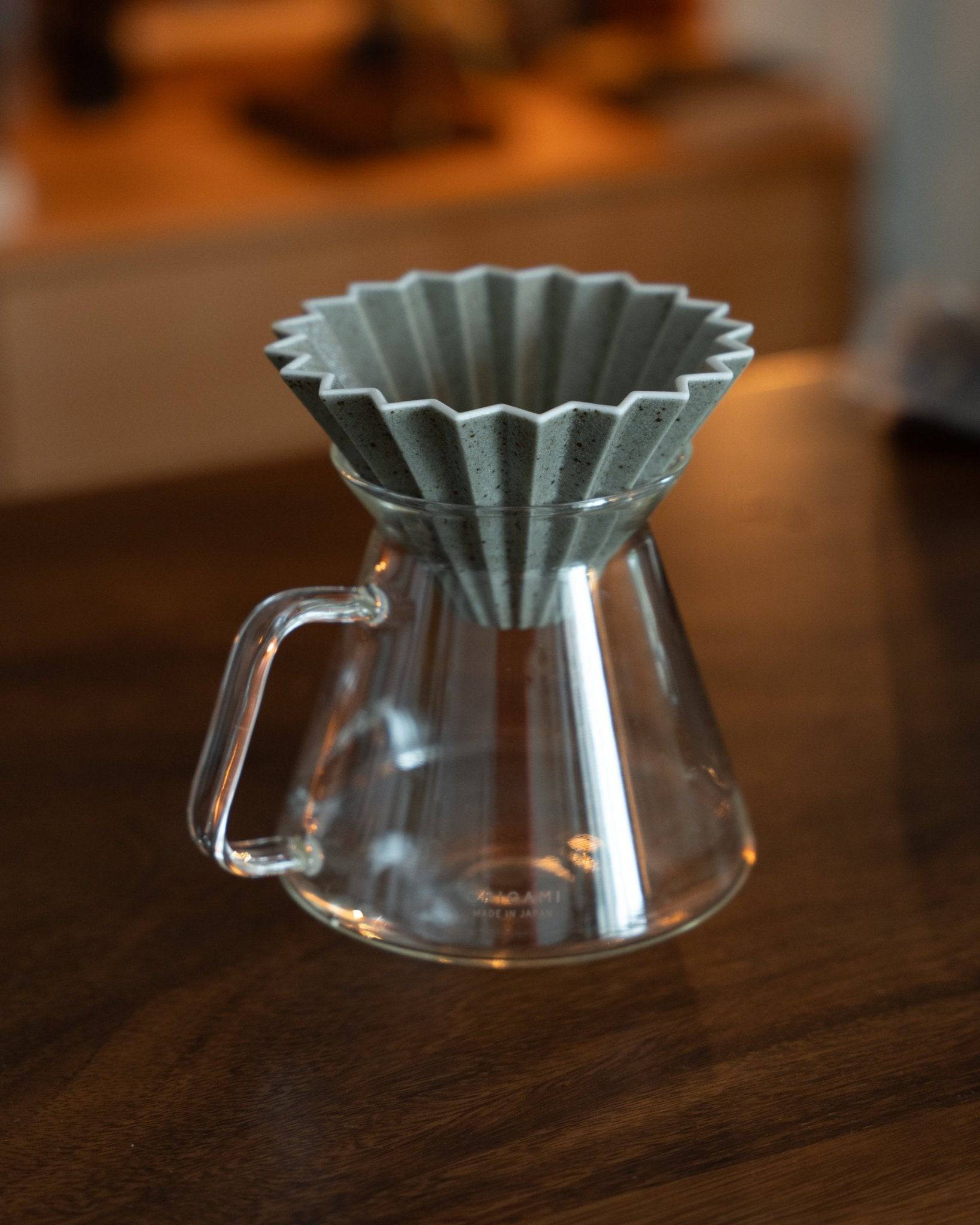 Origami Dripper Mikage limited edition ceramic pour-over coffee filter with unique sandy glaze texture, placed on a glass carafe against a warm wooden background, showcasing Japanese craftsmanship and wabi-sabi aesthetics