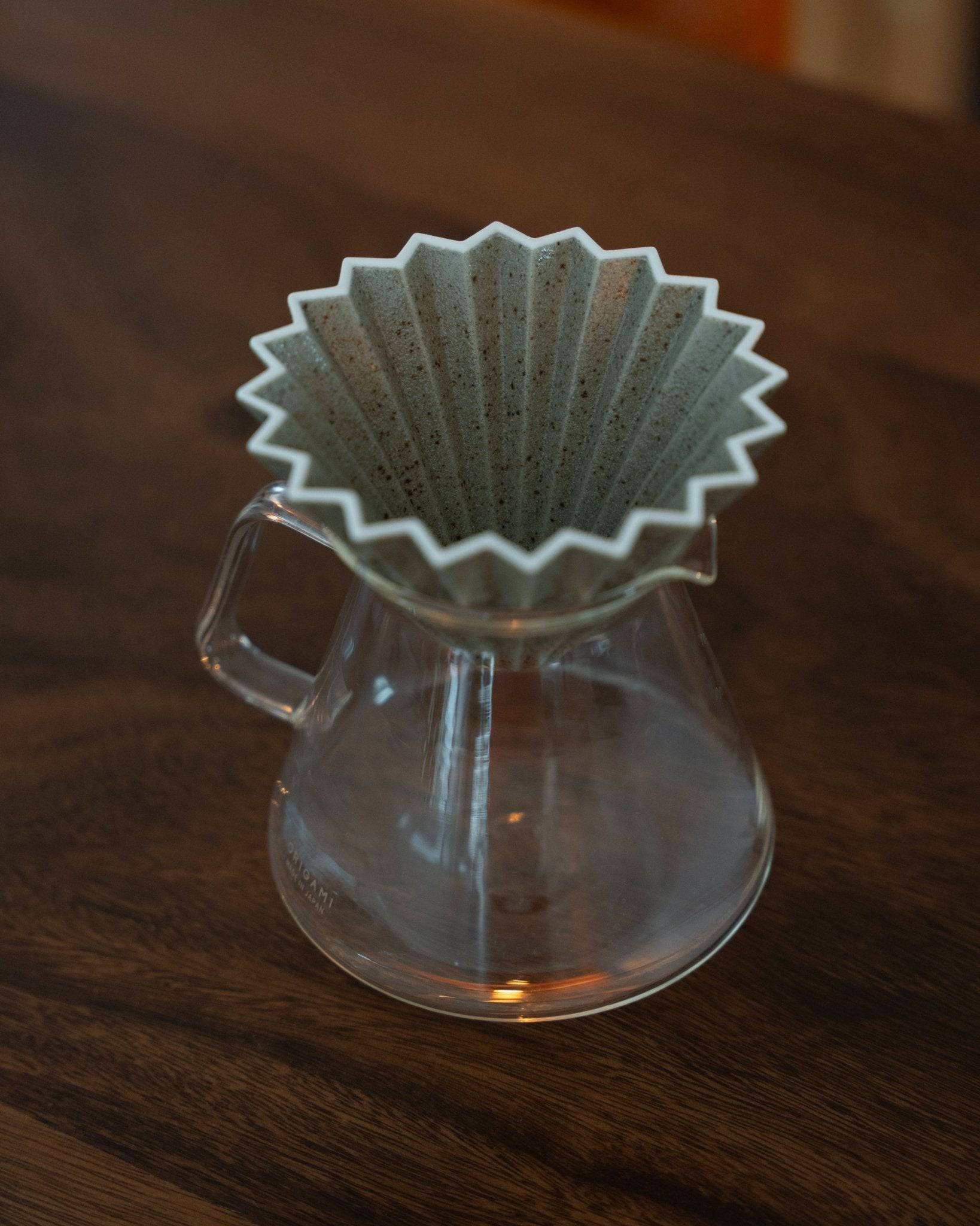 Origami Dripper Mikage limited edition ceramic pour-over coffee filter with unique sand glaze texture atop a glass carafe, showcasing Japanese wabi-sabi aesthetics and craftsmanship