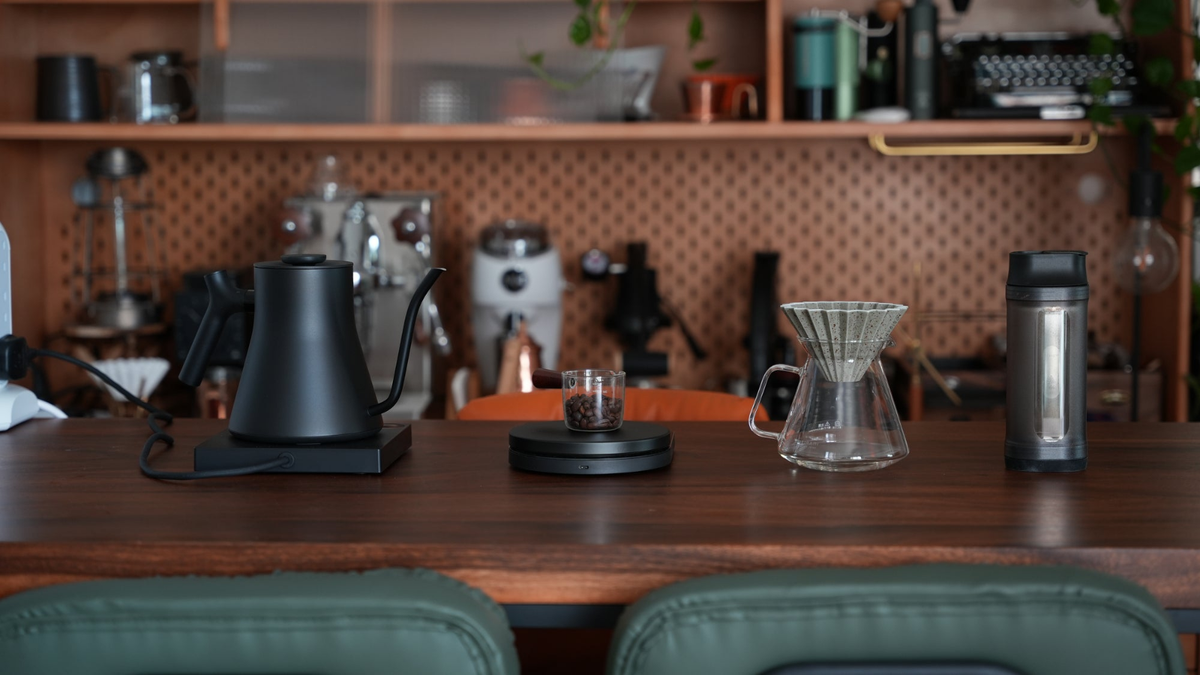 Coffee Stage 過往拍攝的木製咖啡桌，擺放手沖壺、電子磅、玻璃分享壺與濾杯，背景可見其他咖啡器材