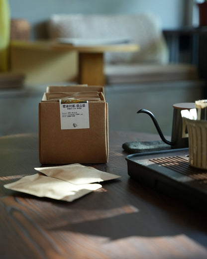 Artisanal coffee packaging and brewing setup on wooden table, featuring cardboard box with Chinese label, pour-over kettle, and coffee filters, showcasing Yunnan CATIMOR 14A coffee product from Sip Coffee.