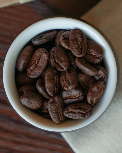 Freshly roasted Yunnan CATIMOR 14A coffee beans in a white ceramic cup, showcasing rich brown color and distinctive bean texture from honey processing method