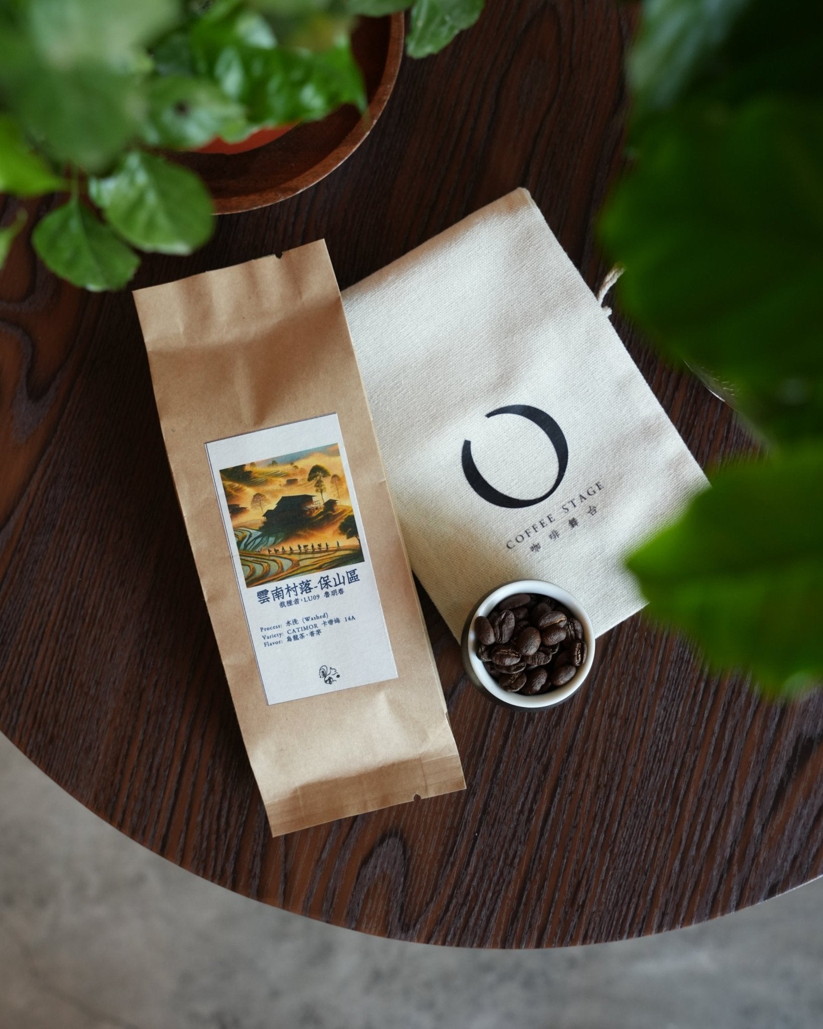 Coffee packaging from Yunnan village displayed on wooden table with coffee beans in small bowl and green plant leaves in frame, showcasing Sip Coffee brand and Catimor 14A product from Baoshan region.