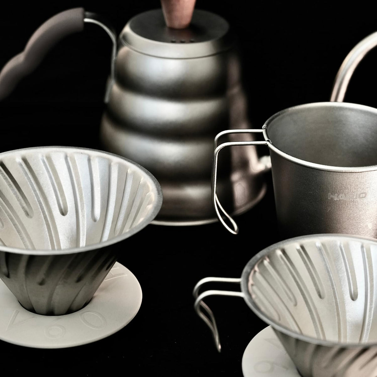 HARIO Titanium 系列合照，展示不同大小濾杯、鈦杯與細口壺的金屬表面