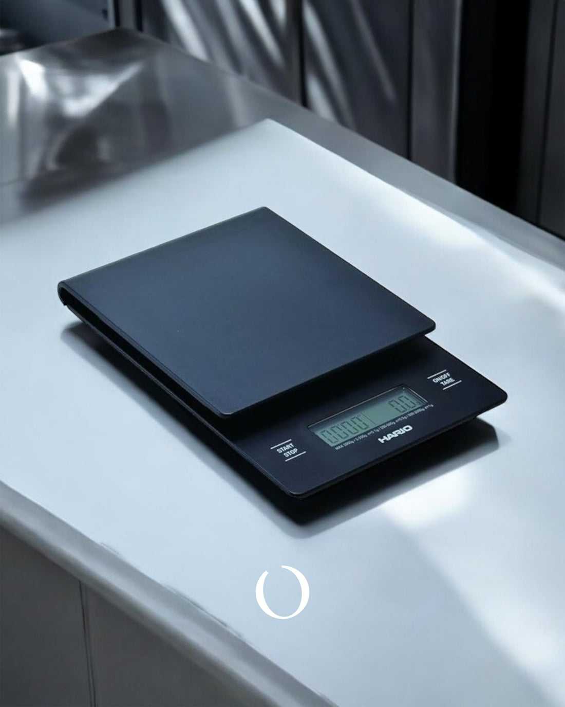 HARIO V60 digital coffee scale on white counter, displaying green LCD screen, sleek black design, precise for pour-over brewing, compact and professional appearance