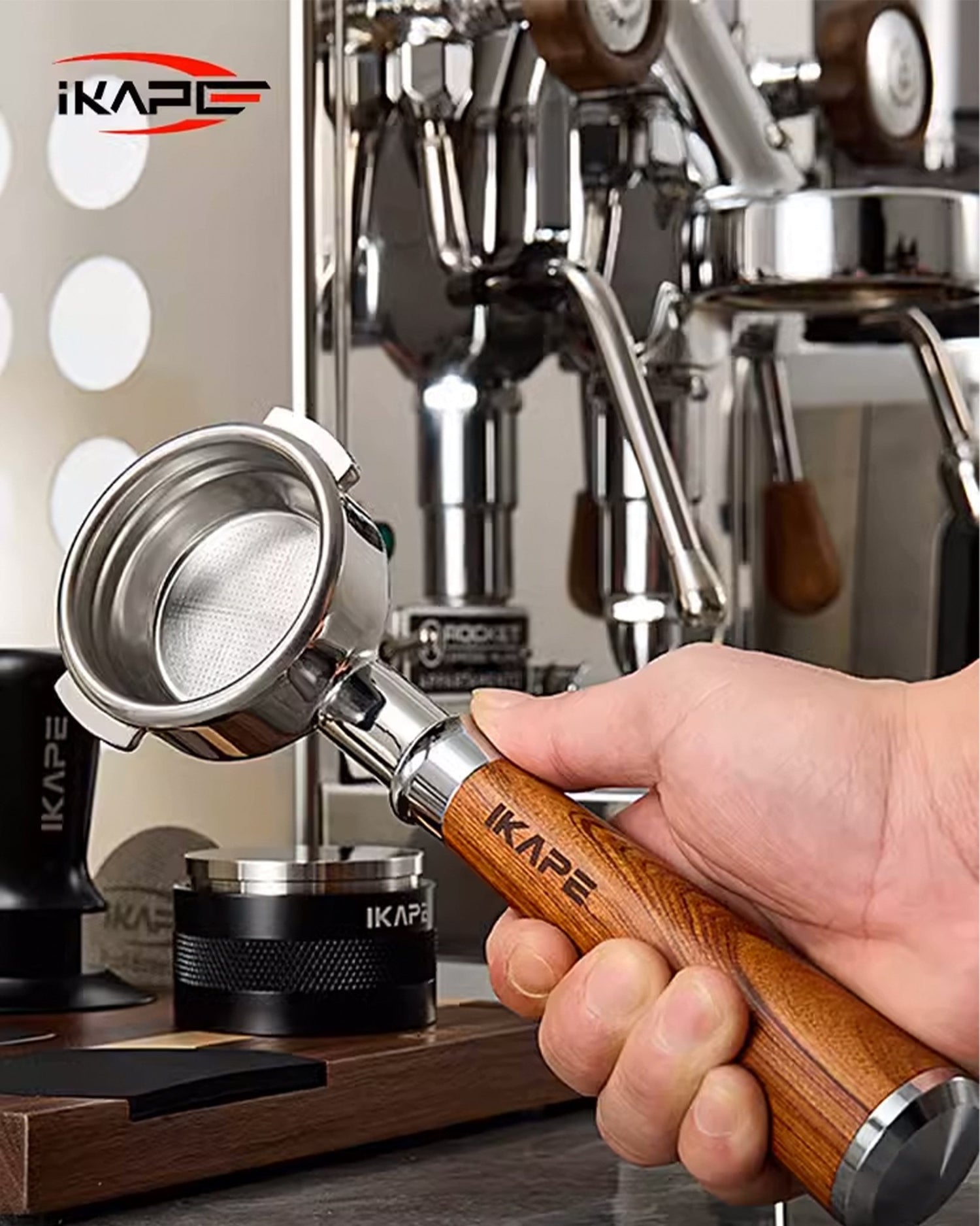 IKAPE bottomless portafilter with wooden handle held by barista near espresso machine, showcasing stainless steel filter basket and brand logo on equipment