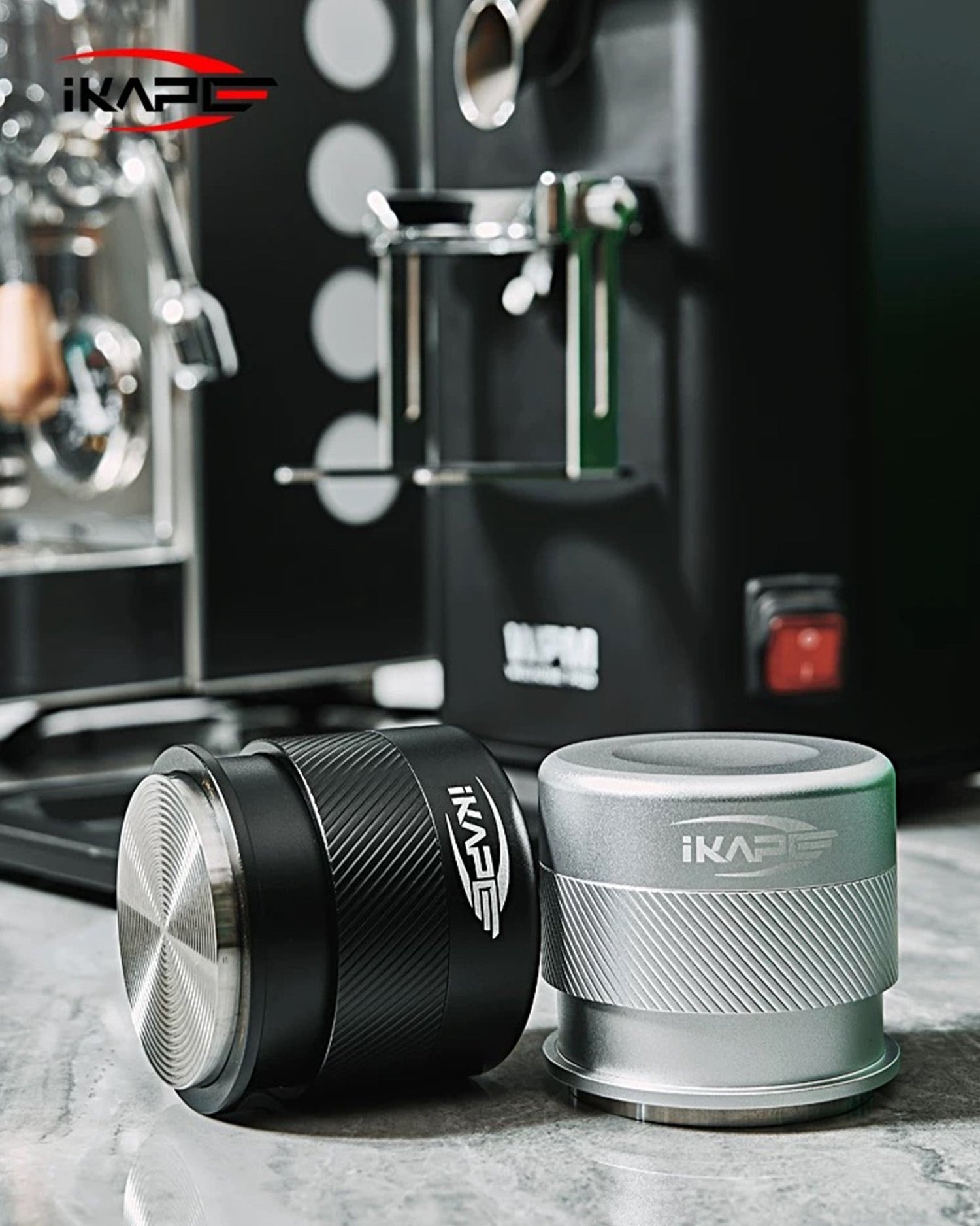 IKAPE Espresso calibrated coffee tampers in black and silver, displayed on marble countertop with espresso machine equipment in background, showcasing professional-grade coffee-making tools