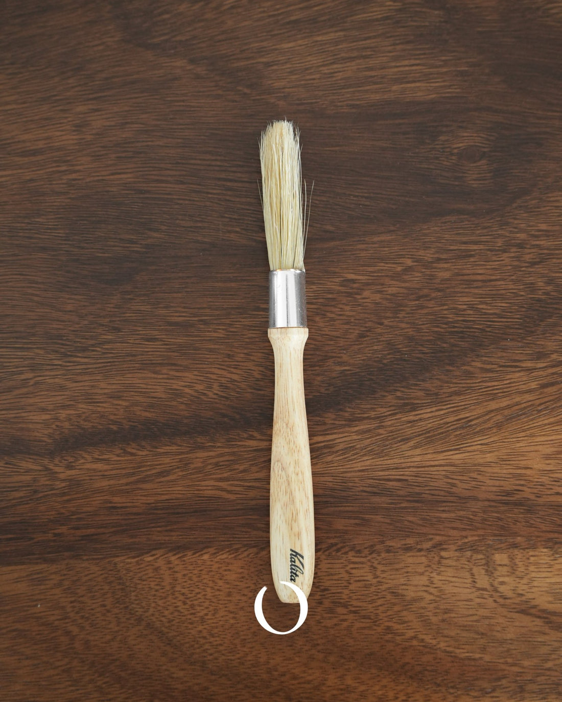 Kalita coffee cleaning brush with wooden handle and bristles, featuring aluminum band and hanging loop, placed on dark wood surface