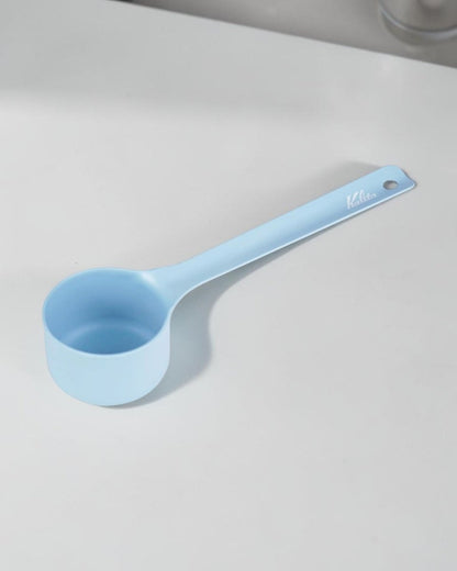 Kalita Earth Series SORA sky-blue stainless steel coffee scoop on a table, showing its long handle, Kalita logo and hanging hole