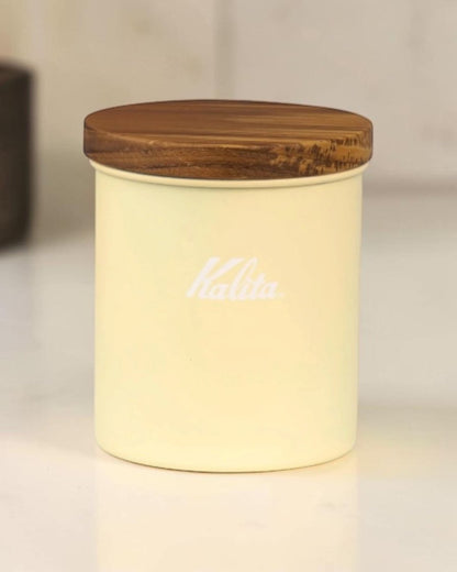 Indoor display of a Kalita Earth Series SUNA sand-coloured stainless steel coffee bean canister with a natural wood lid
