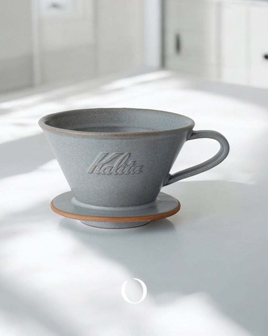 Kalita MI185 Mino ceramic pour-over coffee dripper in gray color, featuring a wide conical shape with handle, placed on a white surface in soft natural light