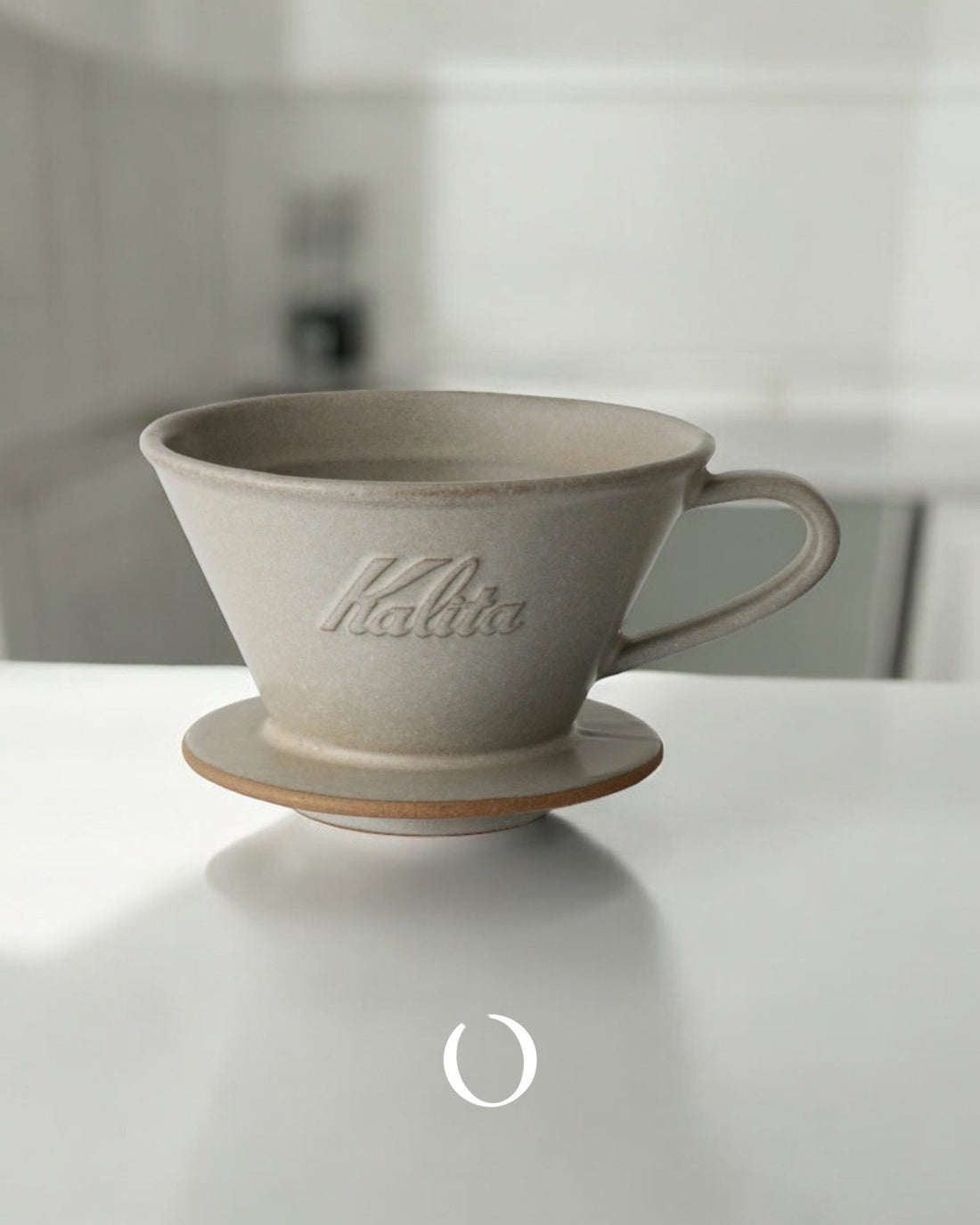 Kalita MI185 ceramic pour-over coffee dripper in light gray, featuring conical shape with embossed logo, handle, and flat bottom design for optimal brewing on white surface