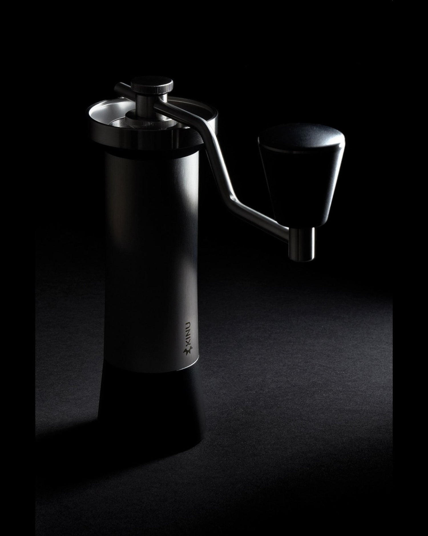 Sleek black Kinu M47 Classic 2024 manual coffee grinder on dark background, highlighting its elegant design and premium stainless steel construction. Ergonomic handle and precision adjustment knob visible, showcasing German engineering and craftsmanship for superior coffee grinding experience.