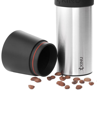 Kinu M47 Phoenix manual coffee grinder with stainless steel body, black lid and cup, surrounded by coffee beans, showcasing portable design for precise grinding on-the-go