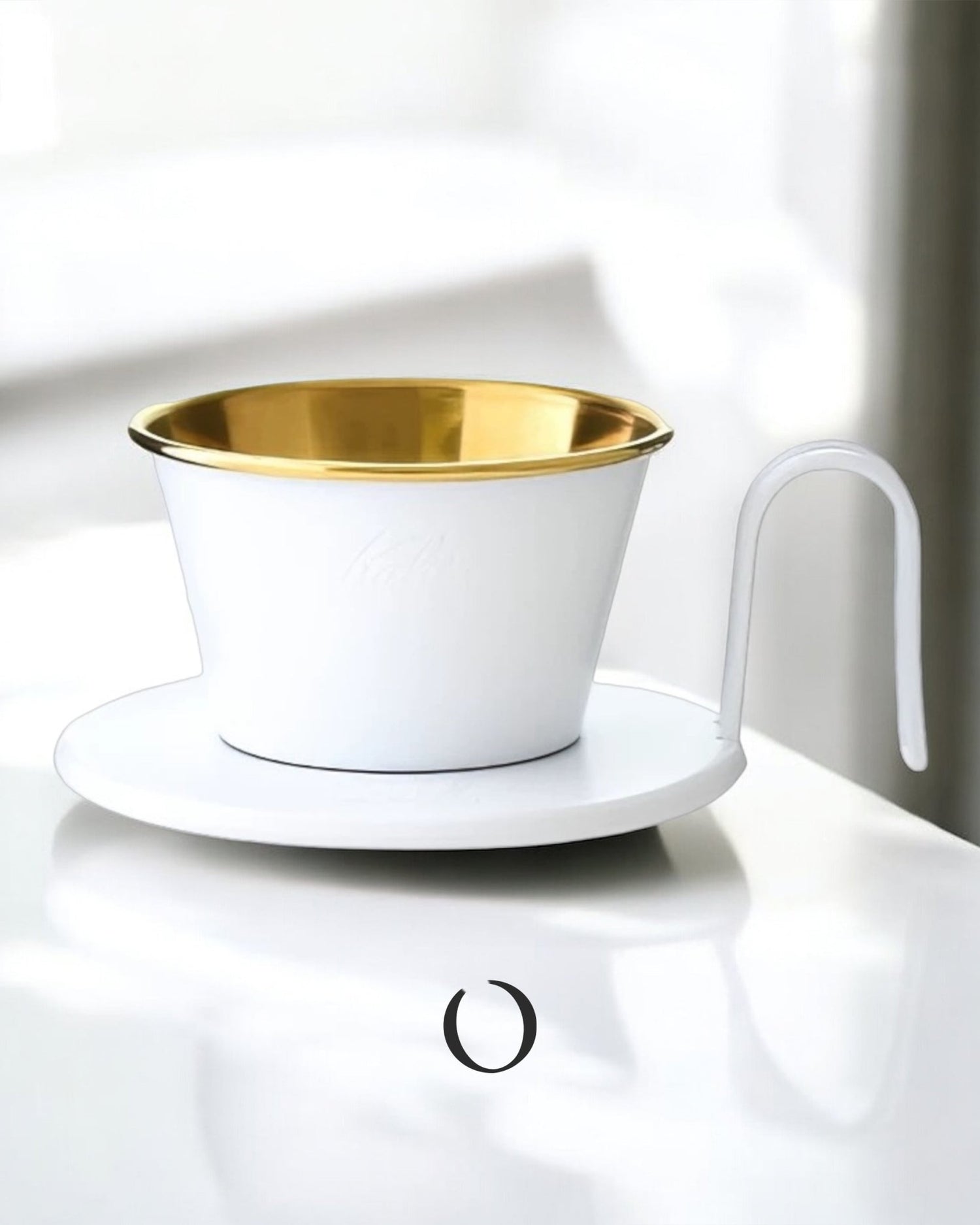 Limited edition Kalita Wave Dripper in white and gold, featuring a unique design with a curved handle and gold interior, positioned on a white saucer against a bright background.