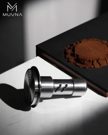 MUVNA 30-pound constant pressure spring tamper V2 with stainless steel base and metal handle, displayed next to coffee grounds on a black surface against a white background