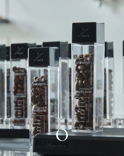 Transparent coffee bean storage tubes filled with various roasts, labeled with roast levels and coffee details, displayed on a sleek stand for presentation and freshness preservation