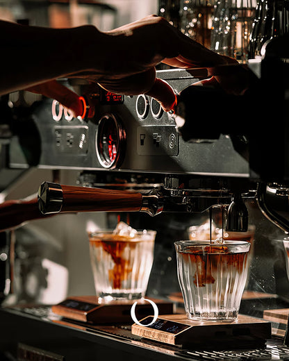 Espresso machine brewing coffee into glass cups, with MUVNA digital scale visible for precise measurement