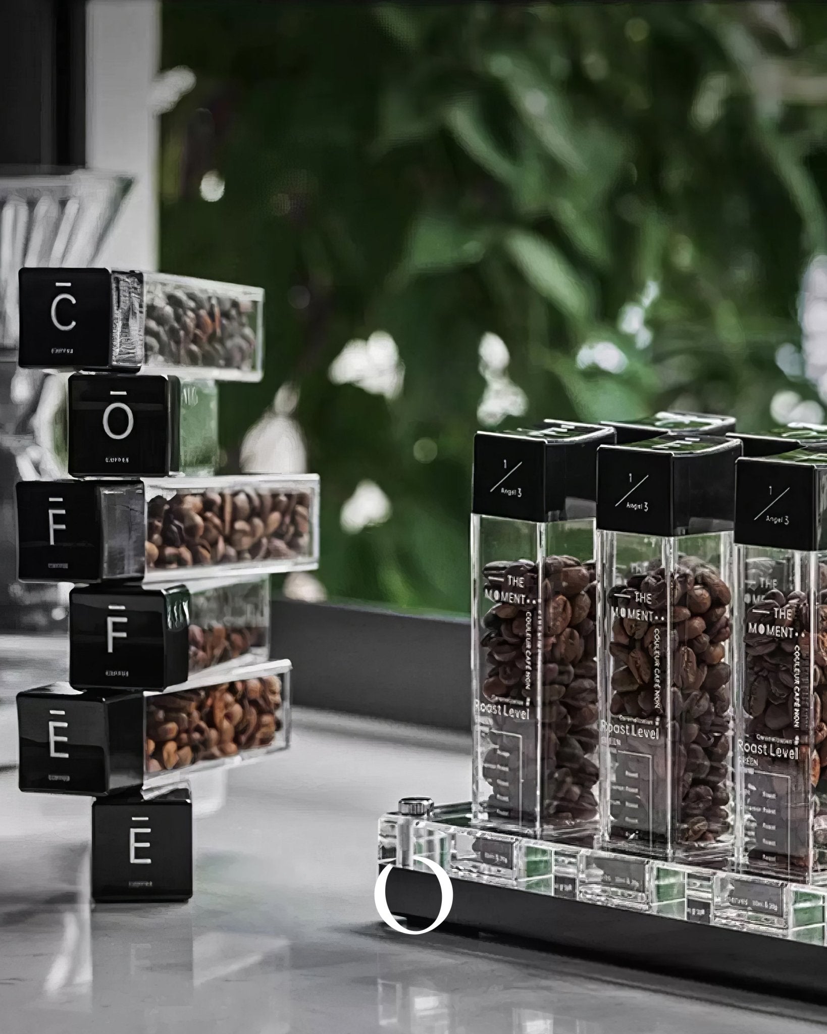 MUVNA coffee bean display tubes and storage system with transparent containers showcasing various coffee beans, arranged on a countertop with a green background