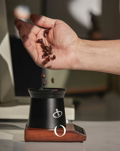 Hand pouring coffee beans into MUVNA walnut wood tilted electronic scale, showcasing precision measurement for coffee enthusiasts