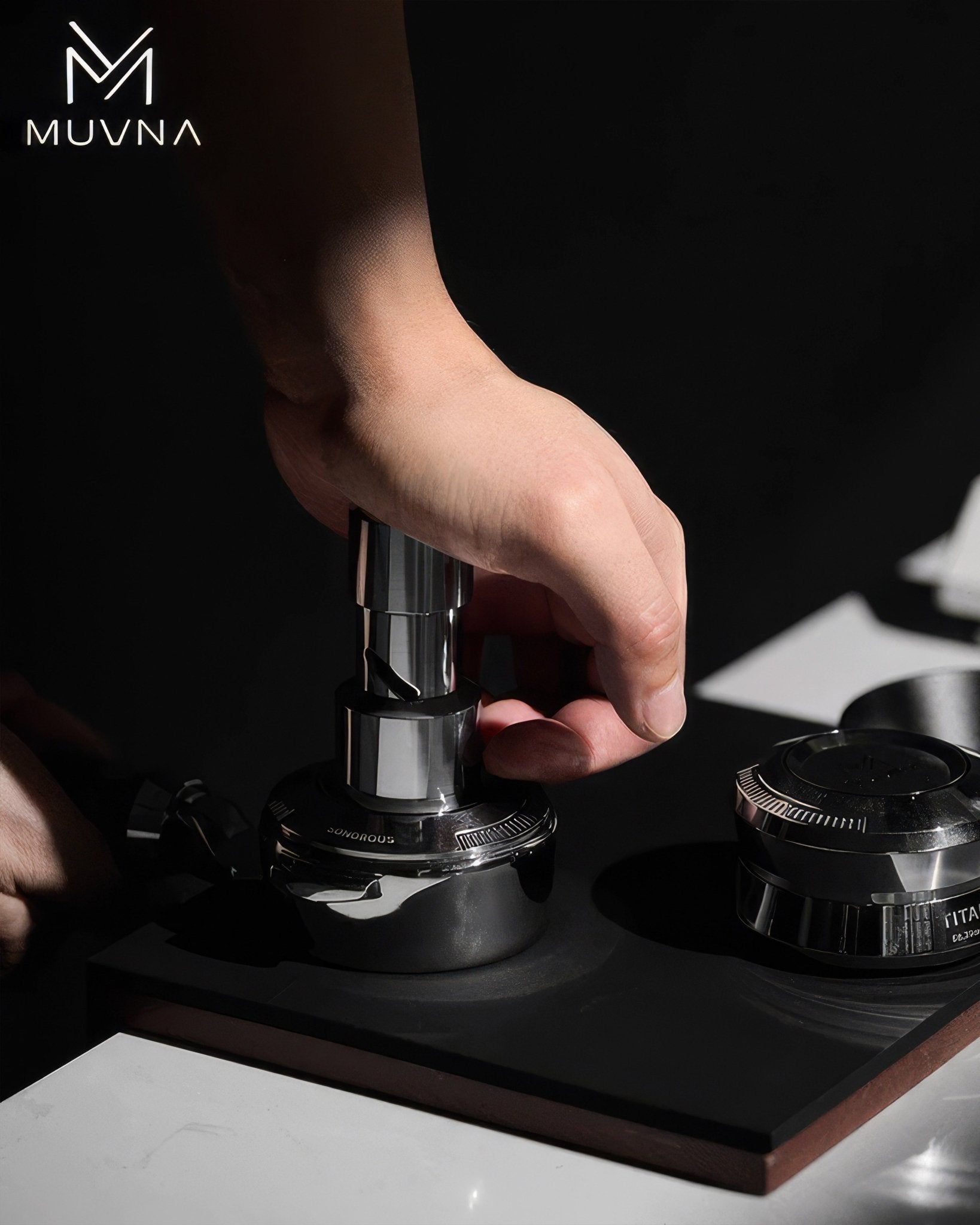 Hand using MUVNA coffee tamper on wooden tamping mat, demonstrating professional espresso preparation technique with high-quality barista tools