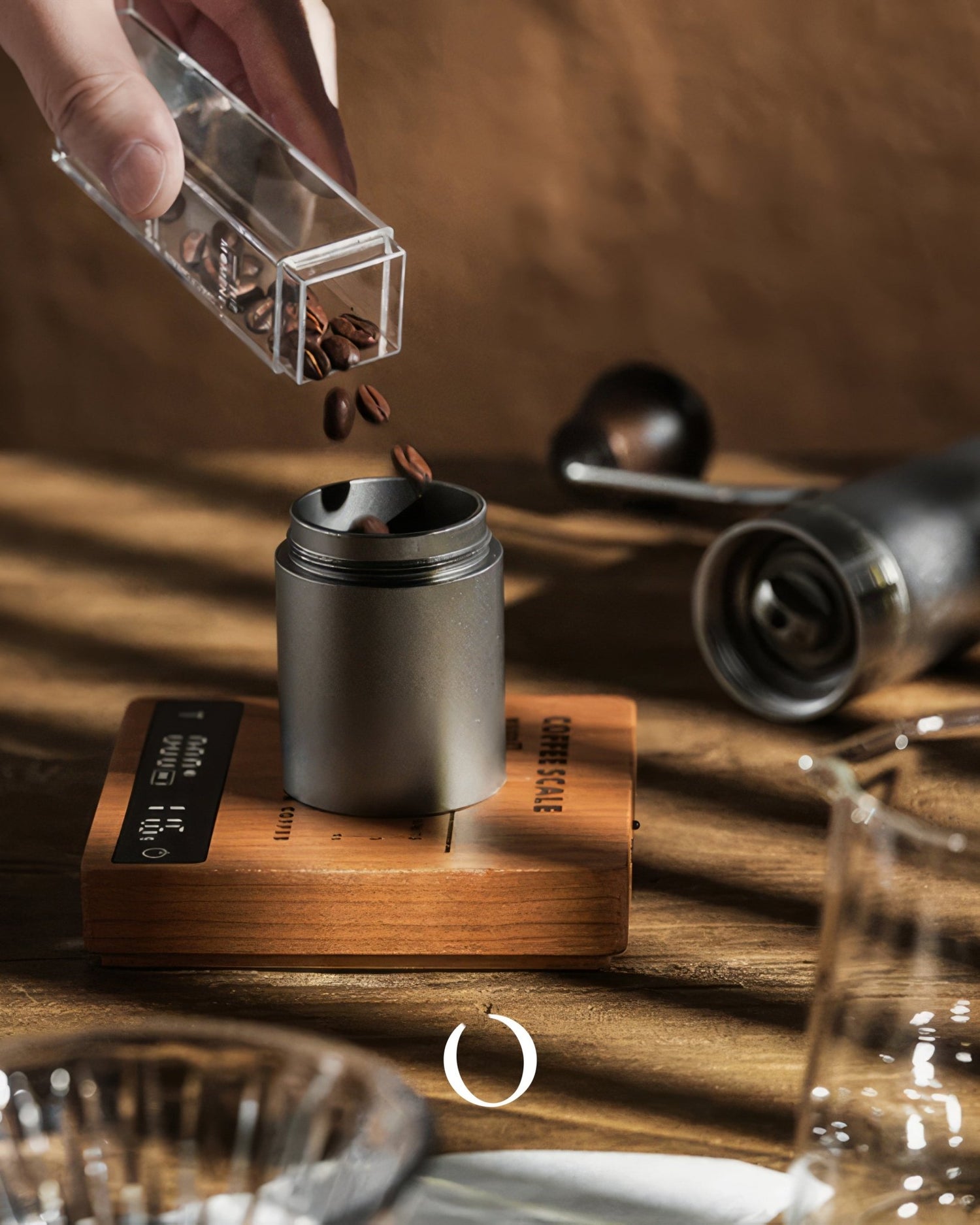 Hand pouring coffee beans into grinder on wooden MUVNA scale, surrounded by coffee brewing equipment on rustic table