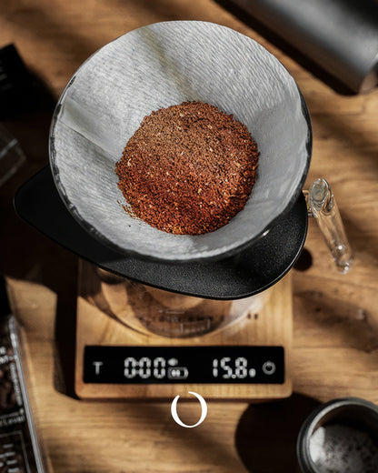 MUVNA walnut wood coffee scale with digital display showing 15.8g of ground coffee in filter, surrounded by brewing equipment on wooden surface, demonstrating precision and elegance in coffee preparation