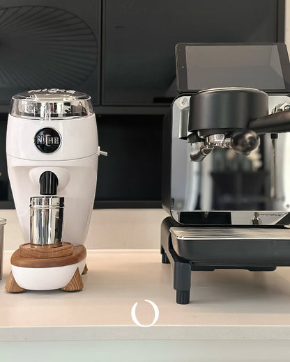 Niche Duo coffee grinder in white next to a silver espresso machine on a countertop, showcasing professional-grade home brewing equipment for coffee enthusiasts