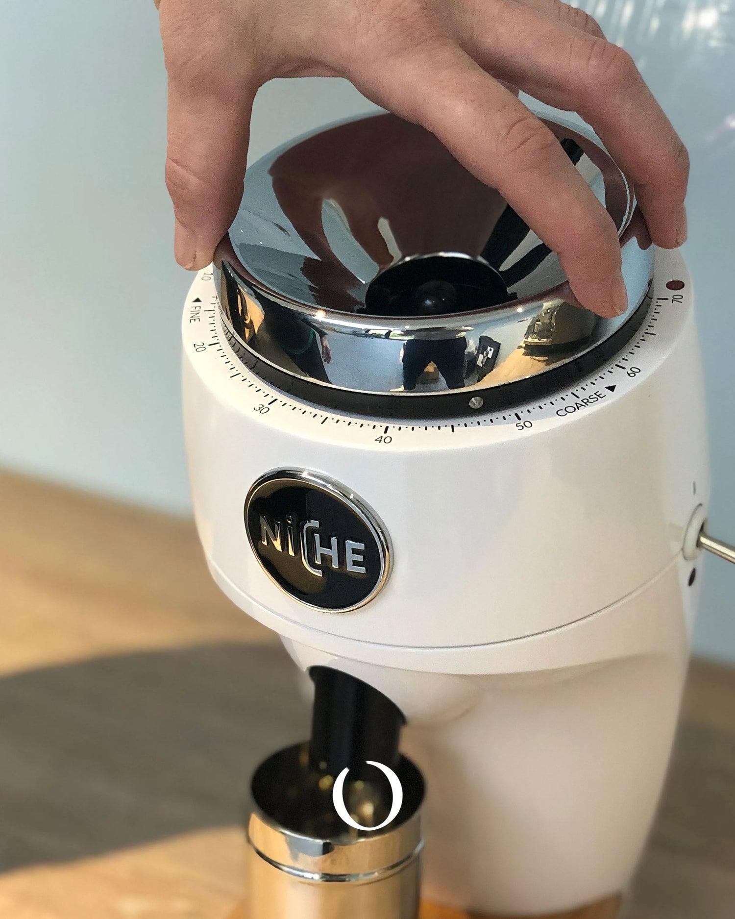 Hand adjusting grind settings on a sleek white Niche coffee grinder, highlighting precise control and professional-grade design for home brewing enthusiasts