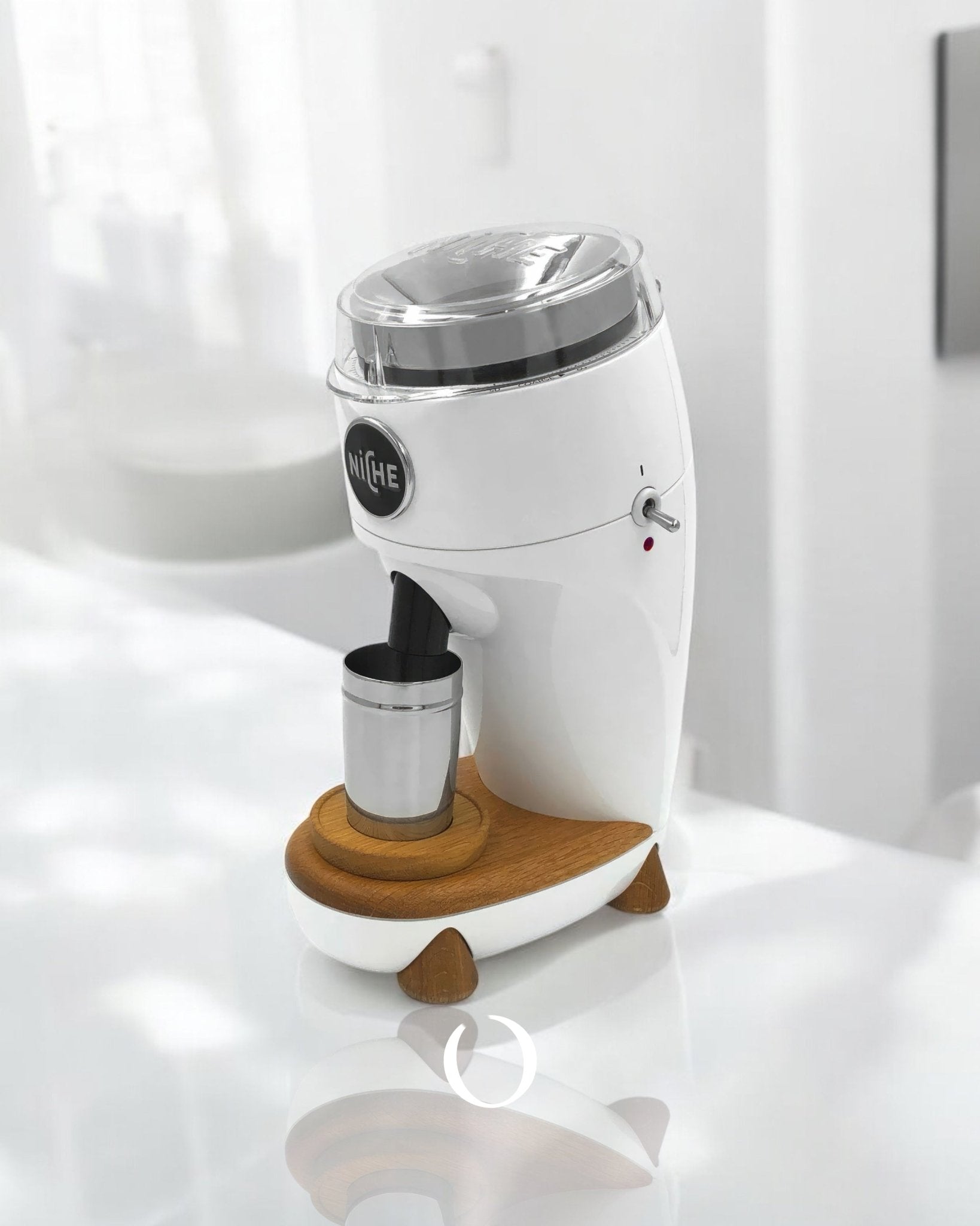 Niche Duo coffee grinder with sleek white design, featuring a metal grinding chamber, wooden base, and steel cup for ground coffee, positioned on a bright surface in a minimalist kitchen setting