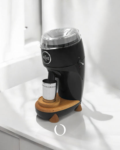 Niche Duo coffee grinder with sleek black design, transparent lid, wooden base, and metal cup positioned on white countertop, showcasing professional-grade home grinding experience