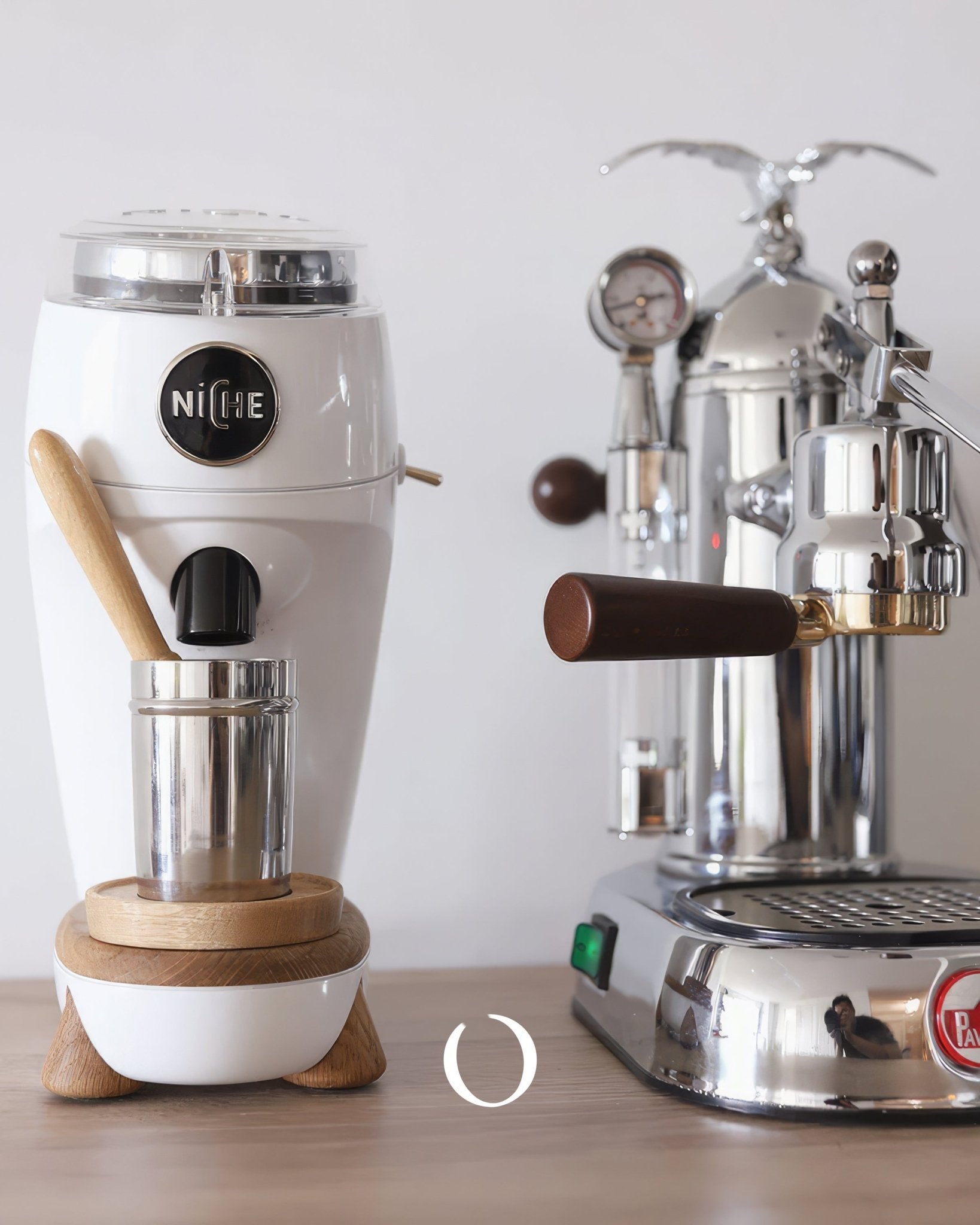 Niche Zero coffee grinder in white with wooden base next to espresso machine, showcasing professional-grade home brewing equipment