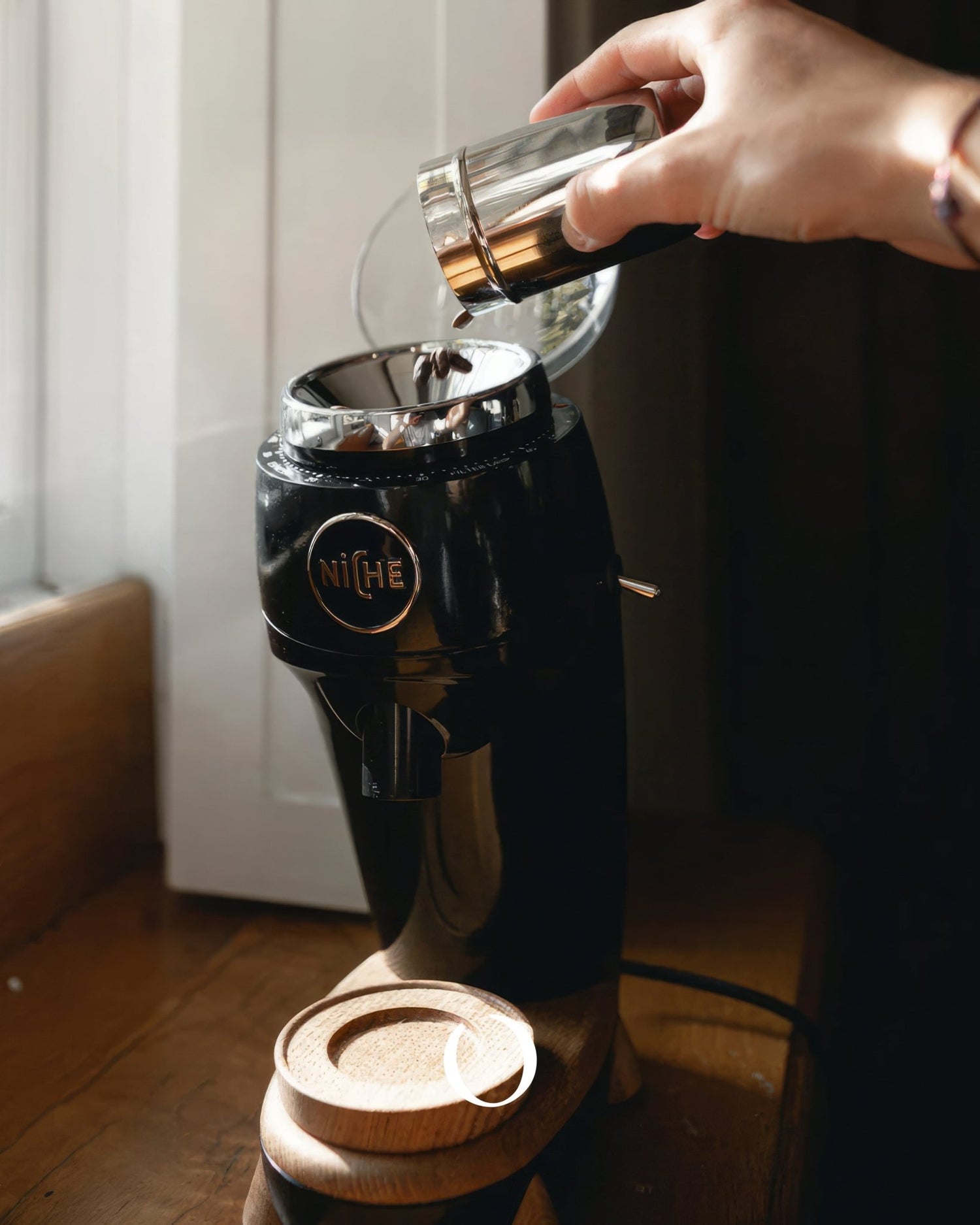 Hand pouring coffee beans into sleek black Niche Zero grinder with wooden base, showcasing precision and quality in home coffee brewing