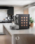 Sleek black Rocket Appartamento TCA espresso machine with distinctive circular side panel design on modern kitchen countertop, showcasing professional-grade features for home baristas.